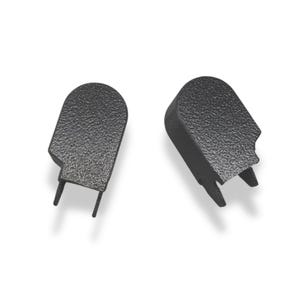 May include: Two black, textured plastic wiper arm covers. Each cover has a rounded top, a rectangular base, and two small prongs extending from the bottom. The covers are designed to protect the wiper arm mechanism.