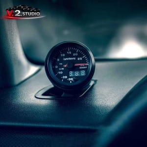 May include: A black Dyno Racing boost gauge with white markings and a digital display showing 8.8.8. The gauge is mounted on a dark dashboard. The gauge reads up to 25 PSI.
