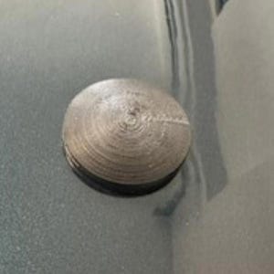 May include: A small, circular, metallic object with a textured, concentric-circle design. The object is a muted silver color and appears to be made of metal. The object is sitting on a reflective surface.