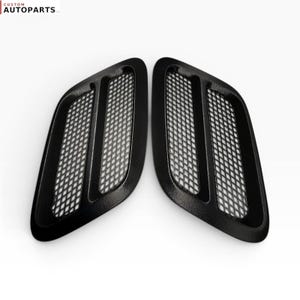 May include: Two black automotive bonnet vents with a textured finish and a diamond-shaped mesh grille pattern. The text CUSTOM AUTOPARTS LLC is visible in the top left corner. These components feature a curved, aerodynamic shape for airflow.