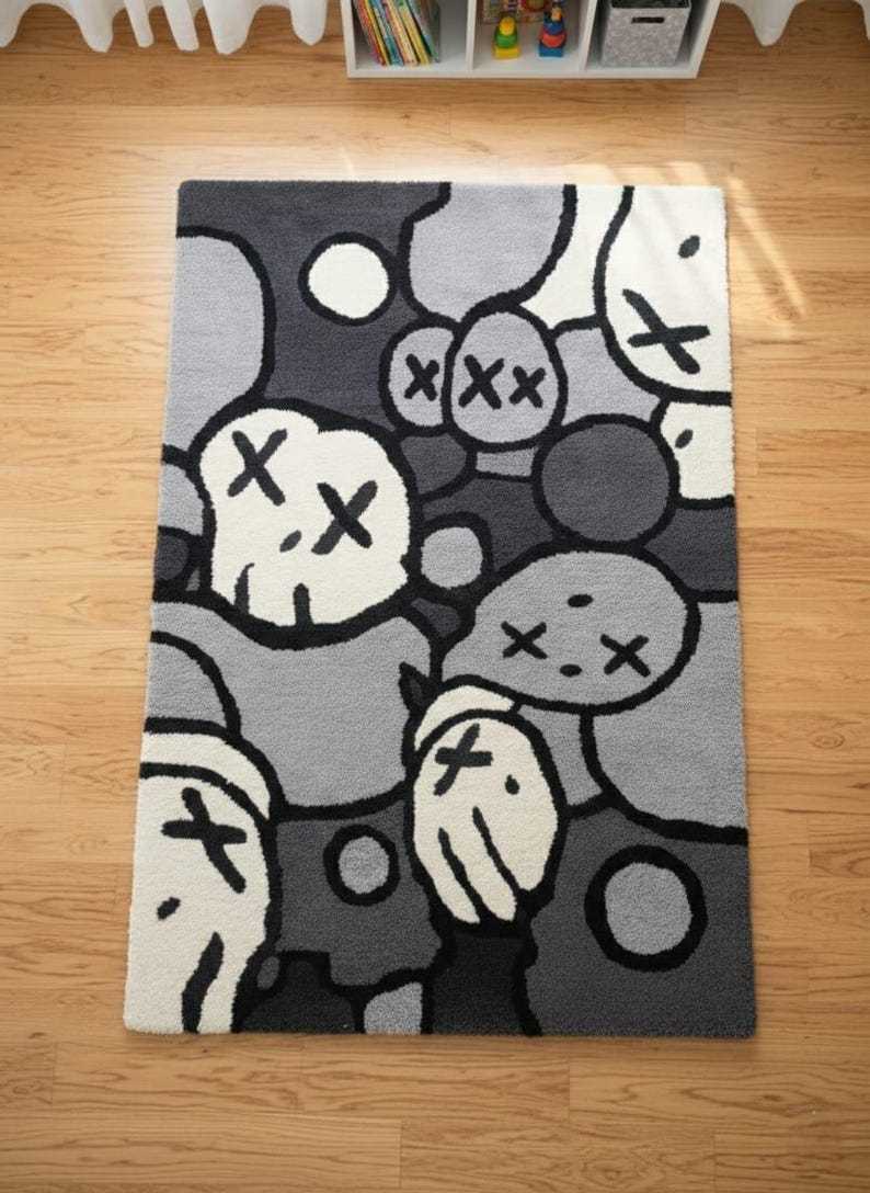 May include: A rectangular rug featuring a repeating pattern of cartoon faces in grey, black, and white. The faces have X-shaped eyes and mouths. The rug is placed on a wooden floor.