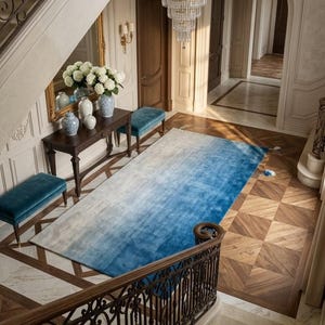 Könnte beinhalten: Ein luxuriöser Eingangsbereich mit einem blau-weißen Ombre-Teppich, einem dunklen Holztisch mit Vasen und Blumen und einem Kristall-Kronleuchter. Der Raum hat eine große Treppe mit einem dekorativen schmiedeeisernen Geländer.