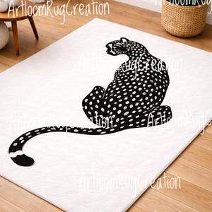 Könnte beinhalten: Weißer rechteckiger Teppich mit einem schwarzen Leopardenmuster mit weißen Punkten. Der Leopard ist sitzend dargestellt, mit ausgestrecktem Schwanz. Der Teppich liegt auf einem Holzboden.