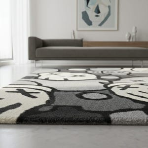 May include: A grey and white patterned rug featuring a repeating cartoon face design. The rug has a plush texture and is in a modern living room. The design includes black outlines and accents.