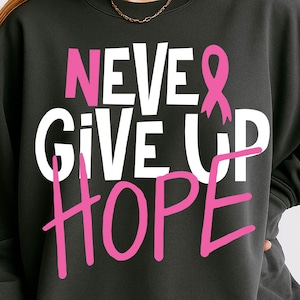 May include: Dark gray sweatshirt with the words "NEVER GIVE UP HOPE" in white and pink lettering. A pink ribbon graphic is included. The sweatshirt is a casual style.
