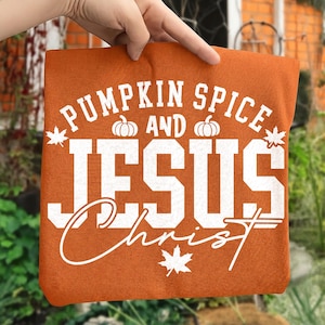 May include: A burnt orange fabric square featuring white screen-printed text that reads PUMPKIN SPICE AND JESUS CHRIST. The design includes two small pumpkin icons and two maple leaf icons, arranged around the bold, block-lettered typography.