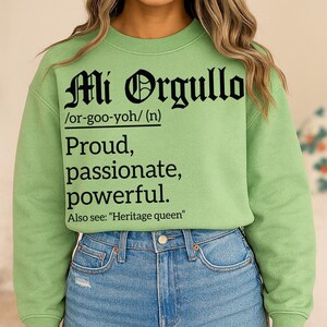 Light green sweatshirt with bold black text reading "Mi Orgullo /or-goo-yoh/ (n) Proud, passionate, powerful. Also see: 'Heritage queen'" in Gothic and serif fonts.