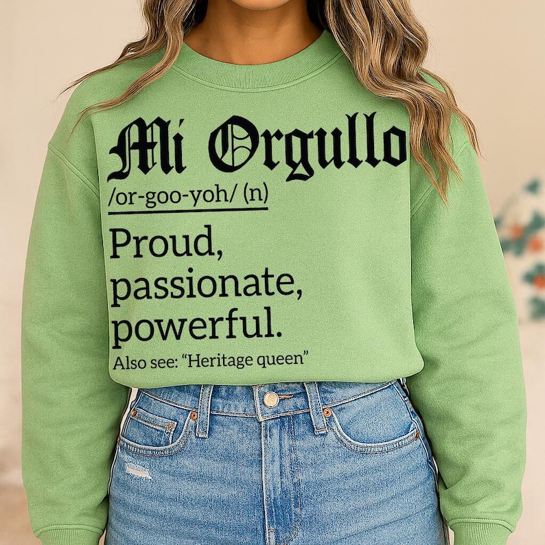 Light green sweatshirt with bold black text reading "Mi Orgullo /or-goo-yoh/ (n) Proud, passionate, powerful. Also see: 'Heritage queen'" in Gothic and serif fonts.