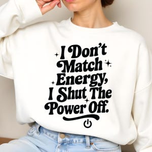 Woman sitting cross-legged in a white crewneck with bold black empowering text “I Don’t Match Energy…” – cozy mockup for digital sassy quote design.