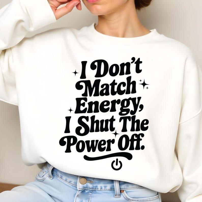 Woman sitting cross-legged in a white crewneck with bold black empowering text “I Don’t Match Energy…” – cozy mockup for digital sassy quote design.
