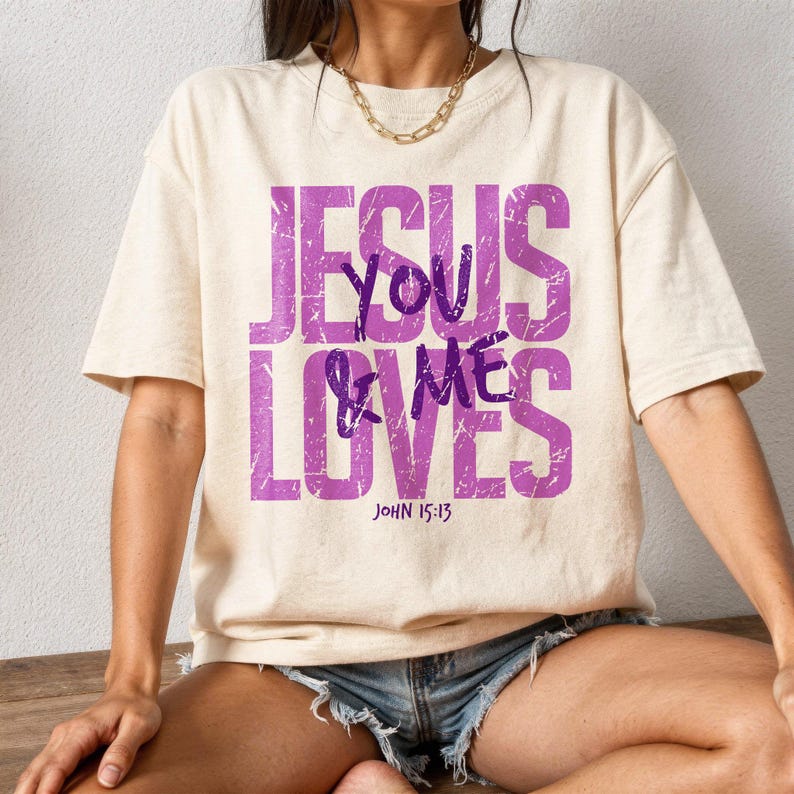 Lifestyle mockup of a woman wearing a cream oversized t-shirt printed with a distressed purple “Jesus Loves You & Me” Christian design and John 15:13 Bible verse. Styled with a gold chain necklace and denim shorts, the outfit creates a modern casual faith look. This mockup showcases inspirational Christian apparel perfect for church outfits, everyday faith wear, and religious shirt listings.