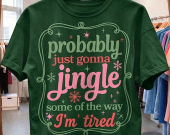 May include: A dark green short-sleeve t-shirt featuring a decorative frame and the text: probably just gonna jingle some of the way I'm tired. The design includes light green, pink, and coral lettering with small star and snowflake accents.