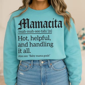 Aqua blue sweatshirt with black text reading “Mamacita /mah-mah-see-tah/ (n) Hot, helpful, and handling it all. Also see: ‘Baby mama goals,’” modeled by a woman in jeans.