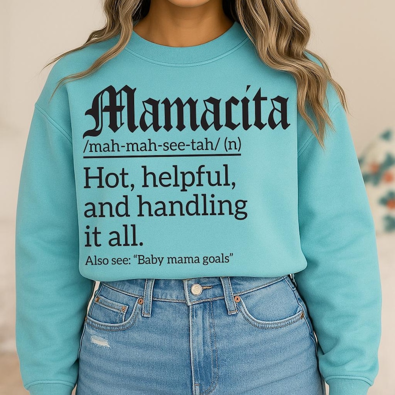 Aqua blue sweatshirt with black text reading “Mamacita /mah-mah-see-tah/ (n) Hot, helpful, and handling it all. Also see: ‘Baby mama goals,’” modeled by a woman in jeans.