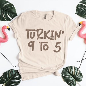 Cream beige Thanksgiving shirt with “Turkin’ 9 to 5” in brown retro font. Cute and funny turkey-themed design inspired by classic song humor. Perfect fall family shirt for cooking day or Friendsgiving events. Trending Thanksgiving PNG for crafting or digital design, great for matching holiday tees and festive fall apparel collections.