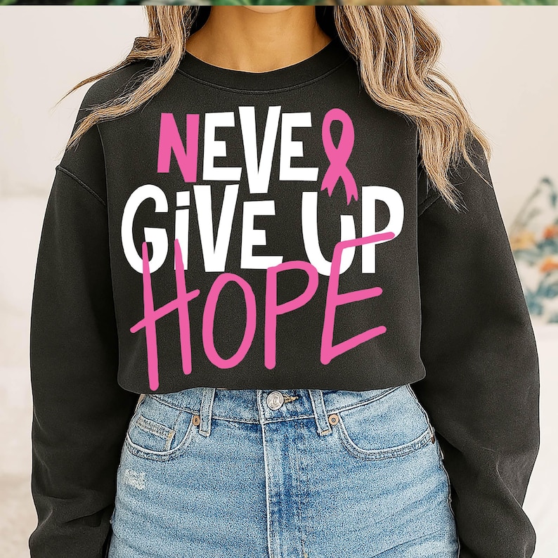 May include: Black sweatshirt with the words "NEVER GIVE UP HOPE" in white and pink lettering. The design includes a pink ribbon, a symbol of breast cancer awareness. The sweatshirt is paired with blue denim jeans.
