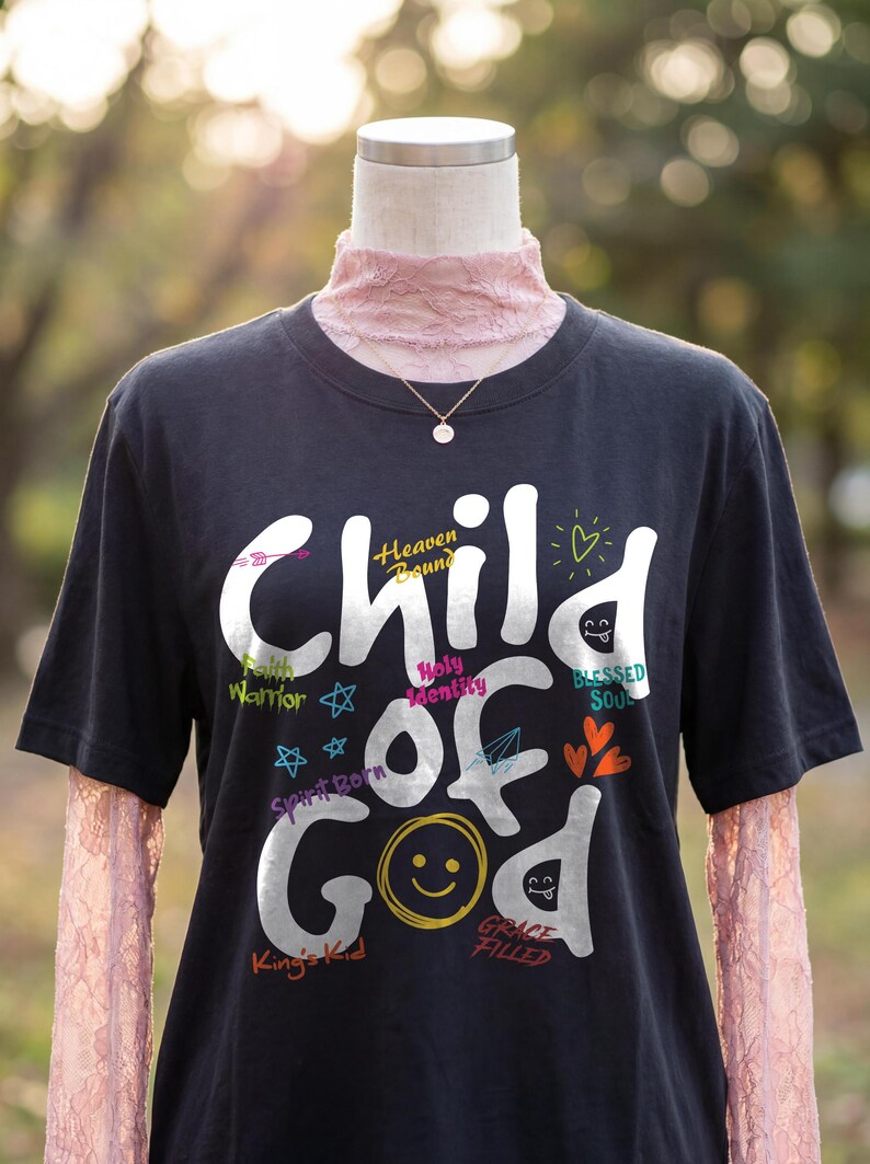 Black Christian t-shirt displayed on a mannequin outdoors, featuring large white “Child of God” lettering surrounded by colorful faith-inspired words like Heaven Bound, Faith Warrior, Holy Identity, Blessed Soul, Spirit Born, King’s Kid, and Grace Filled. Playful doodles, hearts, stars, and a smiley face create a vibrant inspirational church shirt mockup.