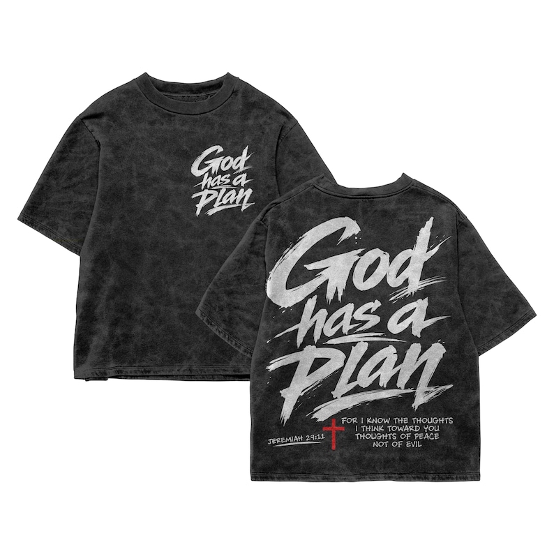 Black acid-wash oversized T-shirt mockup showing both front and back views on a plain white background. The front has a small chest print reading “God has a Plan,” while the back displays the same phrase in large white brush lettering with a red cross, Jeremiah 29:11 reference, and scripture text, creating a modern Christian streetwear design for men.