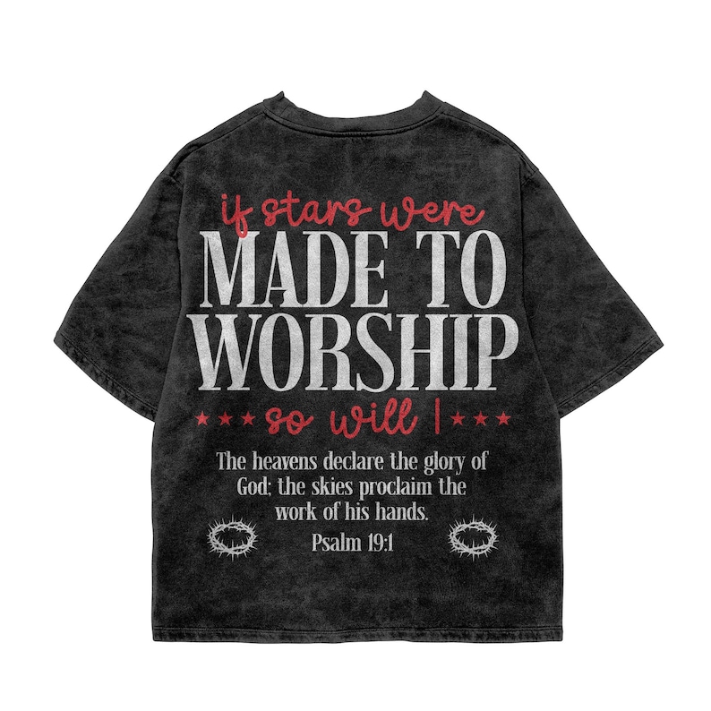 Flat lay mockup of a washed charcoal gray t-shirt featuring a large white and red distressed typographic design. The shirt reads "If stars were made to worship so will I" with "Psalm 19:1" scripture text and crown of thorns graphics at the bottom. A vintage-inspired Christian worship graphic tee designed for everyday streetwear and spiritual inspiration.