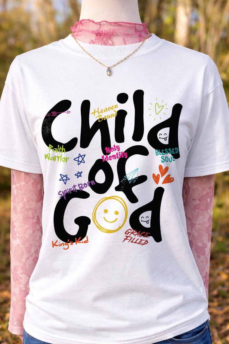 White t-shirt on a mannequin styled with pink lace sleeves and a delicate necklace, showcasing a bold black “Child of God” Christian graphic with colorful handwritten faith phrases and doodle icons. This outdoor mockup emphasizes feminine styling and cheerful inspirational church apparel.