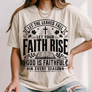 A model wearing a relaxed cream Christian t-shirt paired with ripped jeans and a gold necklace. The front showcases a black vintage emblem reading "Let the Leaves Fall Let Your Faith Rise, God Is Faithful in Every Season, Hebrews 10:23" with an open Bible and cross illustration. Cozy autumn scripture apparel perfect for inspirational daily fashion.