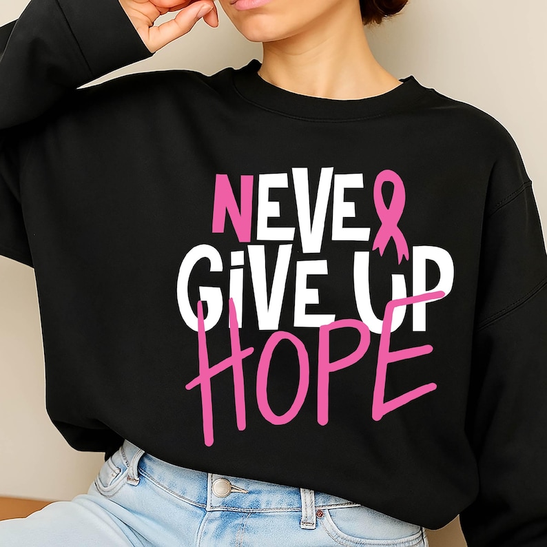 May include: Black sweatshirt with the words "NEVER GIVE UP HOPE" in white and pink lettering. A pink ribbon graphic is incorporated into the design. The sweatshirt is a crew neck style.