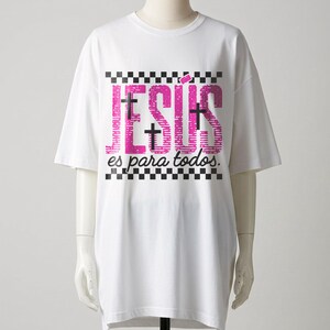 White mannequin display of an oversized Christian graphic t-shirt featuring large pink “JESÚS” lettering with black crosses embedded within the design, framed by checkerboard stripes and finished with “es para todos.” in cursive script. Clean studio presentation highlights this modern Spanish faith apparel design.