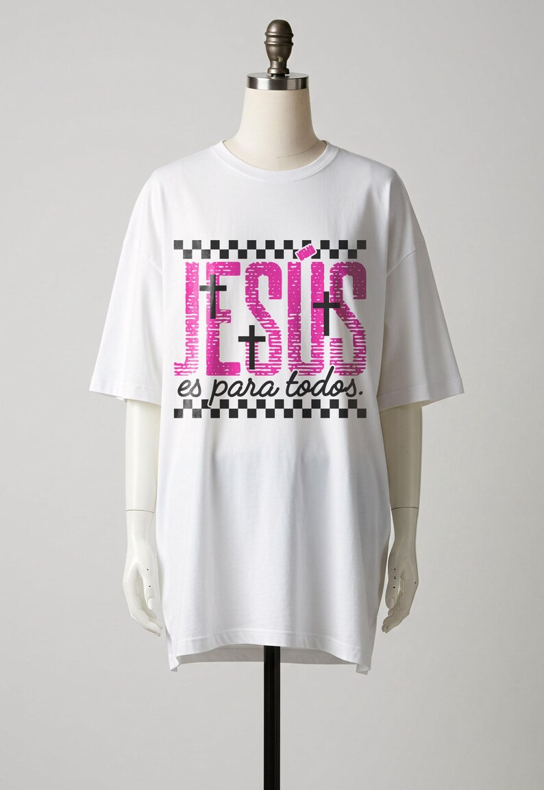 White mannequin display of an oversized Christian graphic t-shirt featuring large pink “JESÚS” lettering with black crosses embedded within the design, framed by checkerboard stripes and finished with “es para todos.” in cursive script. Clean studio presentation highlights this modern Spanish faith apparel design.