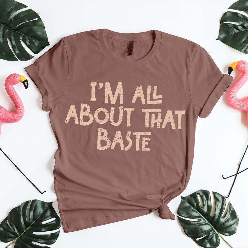 Brown Thanksgiving T-shirt with “I’m All About That Baste” in beige vintage font. Funny holiday cooking shirt for chefs, moms, or food lovers celebrating turkey season. Perfect Thanksgiving outfit for family dinner photos or Friendsgiving parties. Playful fall apparel and Thanksgiving PNG graphic for crafters or sublimation printing projects.