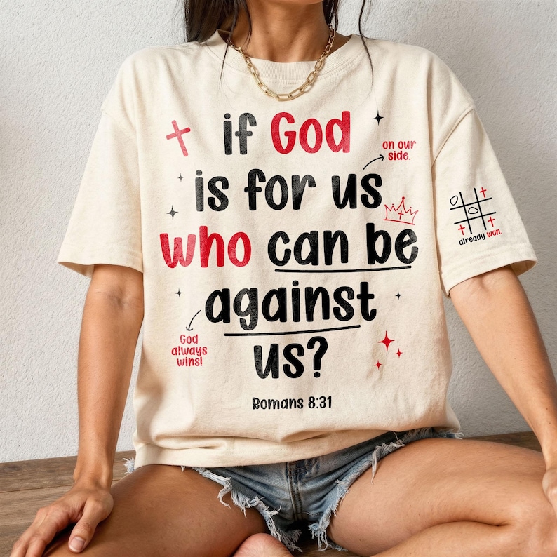 Model wearing an oversized cream Christian t-shirt paired with denim shorts and a gold chain necklace. The front features doodle-style typography reading "If God is for us who can be against us? Romans 8:31" with red accents, crowns, and a tic-tac-toe cross motif on the sleeve. Trendy, casual scripture clothing offering a playful yet powerful message of faith.