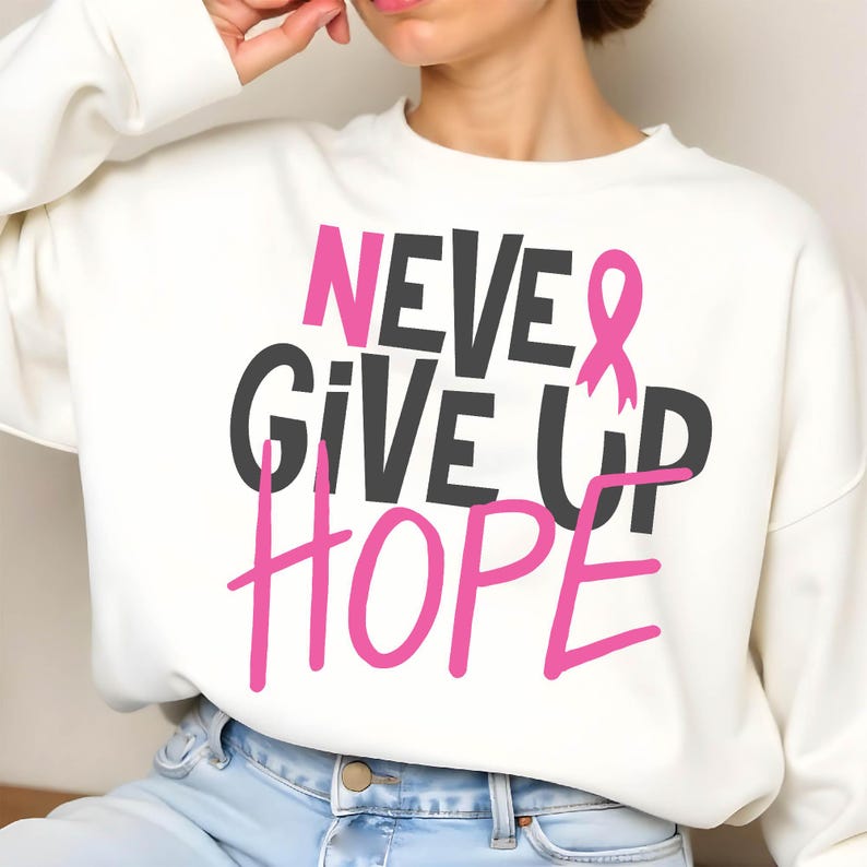 May include: White sweatshirt with the words "NEVER GIVE UP HOPE" in black and pink lettering. A pink ribbon graphic is incorporated into the design. The sweatshirt is a casual style.