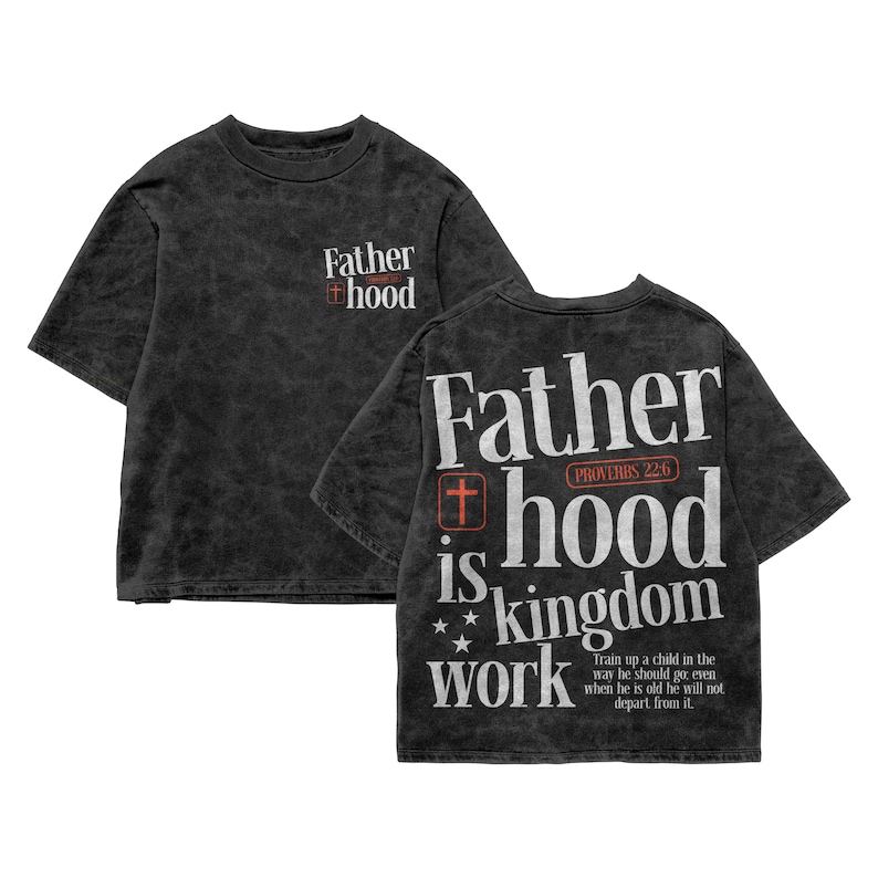 A flat lay showcasing both the front and back design of a dark charcoal vintage mineral wash t-shirt on a white background. The front features a small chest graphic that reads "Father hood" with a red cross icon. The back displays the full, large graphic reading "Father hood is kingdom work" in a distressed white font, accented by a red Proverbs 22:6 emblem, small stars, and the full biblical scripture quote.