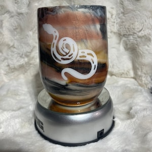 Può includere: Una tazza in ceramica marrone e bianca con un motivo a spirale e un design a serpente bianco. La tazza è su un supporto rotante argentato.