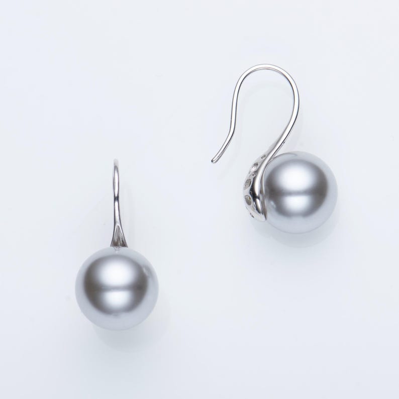 May include: A pair of silver drop earrings featuring large, lustrous gray pearls. The earrings have a simple, elegant design with a curved hook and a decorative element near the pearl. The pearls are approximately 0.5 inches in diameter.