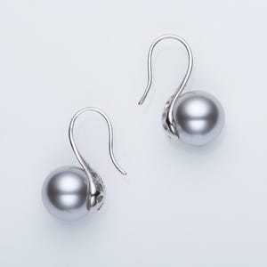 May include: A pair of silver drop earrings with large, gray, spherical pearls. The earrings have a curved hook design with a decorative element near the pearl. The background is a clean, white surface, highlighting the jewelry.