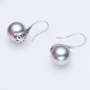 May include: A pair of silver-toned drop earrings featuring large, gray, spherical pearls. The earrings have a decorative, openwork design on the back of the pearl setting and a curved hook for pierced ears.
