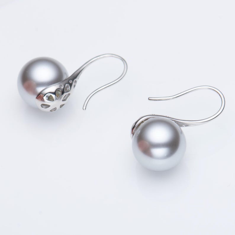 May include: A pair of silver-toned drop earrings featuring large, gray, spherical pearls. The earrings have a decorative, openwork design on the back of the pearl setting and a curved hook for pierced ears.