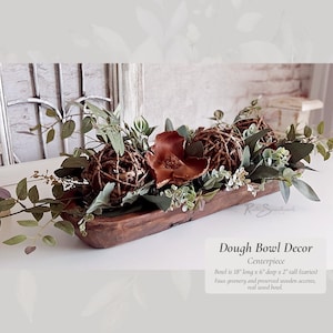 May include: A rustic wooden dough bowl centerpiece decorated with faux greenery, preserved wooden balls, and brown accents. The bowl is 18 inches long, 6 inches deep, and 2 inches tall. "Dough Bowl Decor Centerpiece" is written in the image.