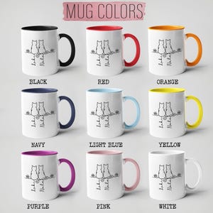 May include: White ceramic mugs with colored handles and interiors, featuring a black line drawing of two cats and the text "Loki & Nala." The mugs come in various colors, including black, red, orange, navy, light blue, yellow, purple, pink, and white.