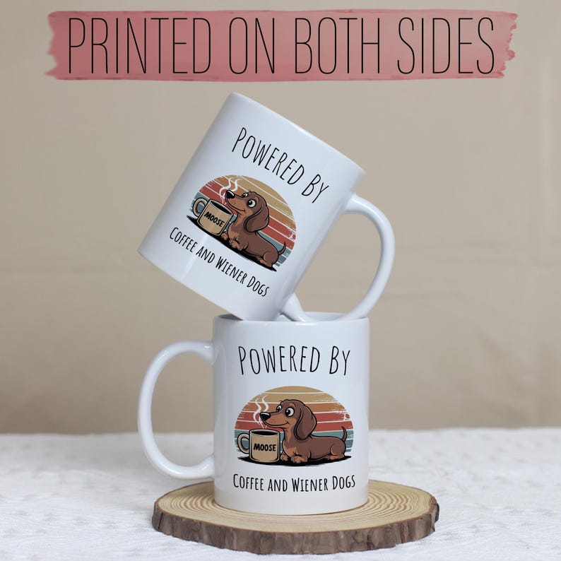 May include: Two white ceramic mugs stacked on a wooden coaster. Each mug features a dachshund illustration with the text "POWERED BY COFFEE AND WIENER DOGS." The mugs have a curved handle and a retro sunset design.
