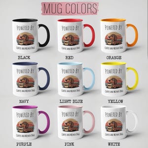 May include: Collection of white ceramic mugs with different colored rims and handles. Each mug features a dachshund illustration and the text "POWERED BY Coffee and Wiener Dogs". Colors include black, red, orange, navy, light blue, yellow, purple, pink, and white.