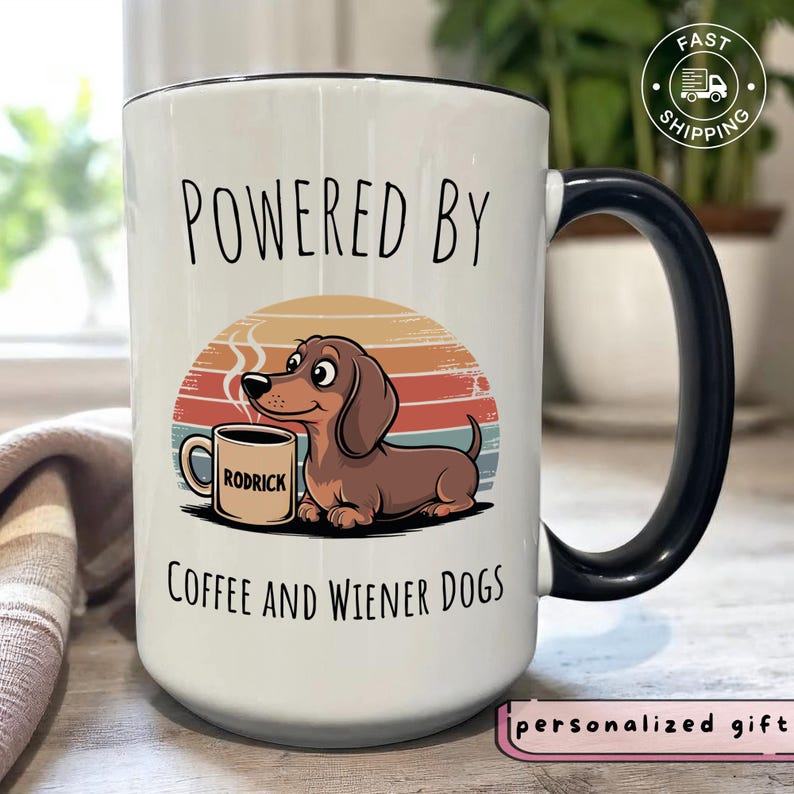 May include: White ceramic mug with a black handle and rim. The mug features the text "POWERED BY COFFEE AND WIENER DOGS" with a cartoon dachshund and a coffee cup. The coffee cup has the name "RODRICK" on it.