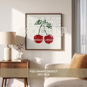 May include: A square wooden picture frame hanging on a wall, displaying a print of two red cherries with green leaves. The frame is centered above a wooden nightstand with a lamp and a small vase. The text FRAME MOCKUP is overlaid in white.