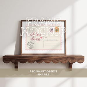 Pode incluir: Uma moldura de madeira retangular contendo uma impressão de cartão-postal com uma borda rosa recortada. A impressão apresenta o texto "with love, always" em letra cursiva rosa, um pequeno coração, dois selos e um carimbo postal circular em tinta preta.