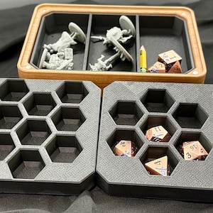 May include: A wooden and gray dice and miniature organizer. The organizer has multiple compartments, including honeycomb-shaped trays for dice and rectangular sections for miniatures. A yellow pencil is also visible.