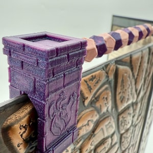 May include: A purple, 3D-printed miniature castle wall section with a decorative flame emblem. The wall features a textured stone design in shades of brown and tan. A series of purple and tan geometric shapes form a decorative element.