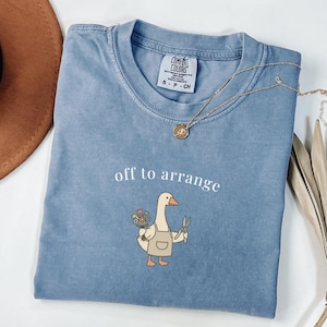 Blue Comfort Colors t-shirt with "off to arrange" and a goose holding flowers and scissors.