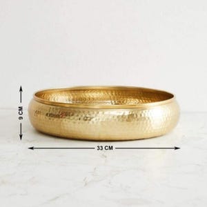 以下が含まれることがあります： ハンマー加工された金色の金属製のボウル。ボウルの直径は33cm、高さは9cmです。丸みを帯びた形状とテクスチャ加工された表面を持っています。装飾目的で使用される可能性があります。