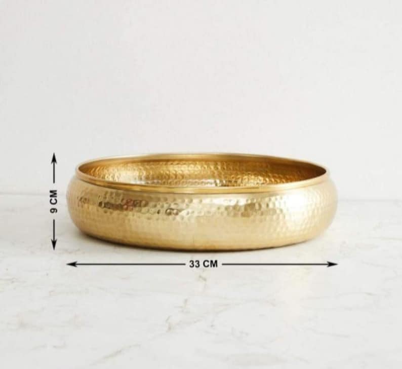 以下が含まれることがあります： ハンマー加工された金色の金属製のボウル。ボウルの直径は33cm、高さは9cmです。丸みを帯びた形状とテクスチャ加工された表面を持っています。装飾目的で使用される可能性があります。