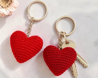 May include: Two red crocheted heart keychains with gold-colored key rings and chains. One keychain has two keys attached. The text "By Mama And Stitches" is in the upper right corner.